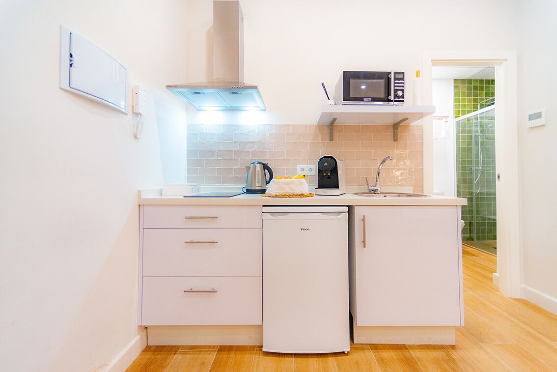 Cocina compacta equipada con lavavajillas, microondas y tetera.