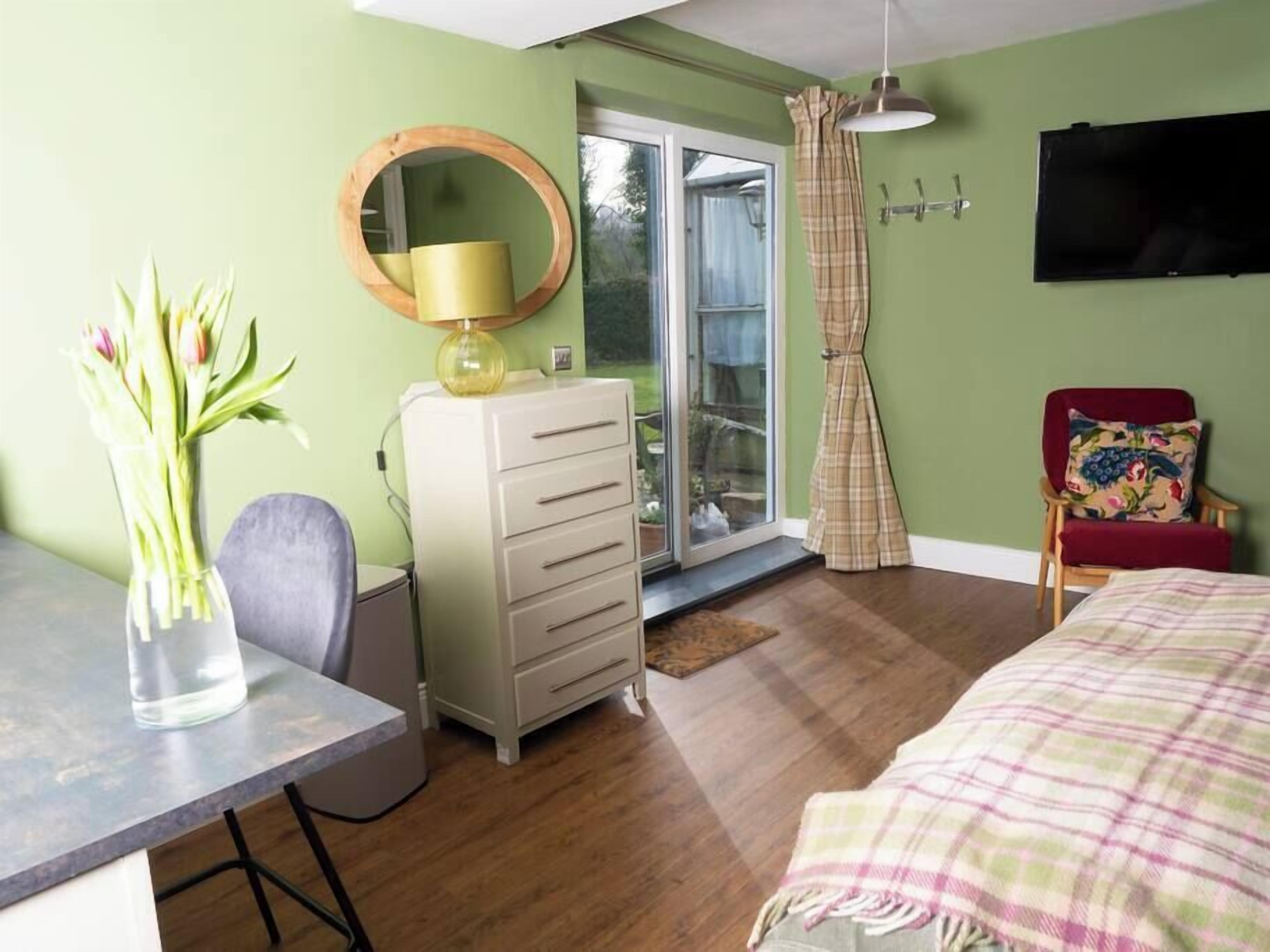 A bedroom with a bed, a dresser, a chair, a desk with a lamp, and a window with curtains.