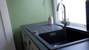 Una cocina con un lavamanos negro, una ventana y una pared verde.