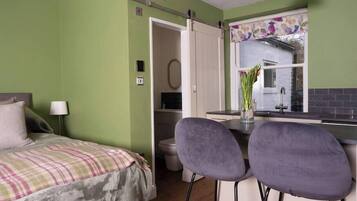 Een compacte kamer met een bed, twee barstoelen, een kitchenette en een raam met uitzicht.
