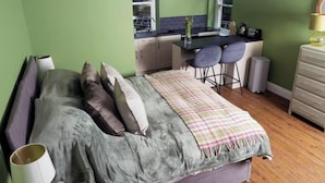 Un dormitorio con cama, mesita de noche, lámpara y vistas a una cocina con mesa y sillas.