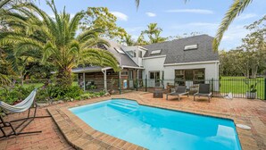 Una proprietà residenziale con piscina, area relax esterna e giardino con piante tropicali.