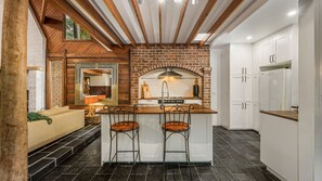 A kitchen with a brick backsplash, wooden ceiling beams, a bar area with stools, and white cabinetry.