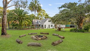 Una casa con un focolare circolare in pietra circondato da tronchi, un cortile recintato e diversi alberi.