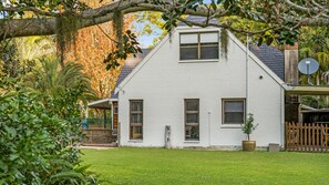 A white two-story house with a sloped roof, a satellite dish, and a fenced yard with a lawn.