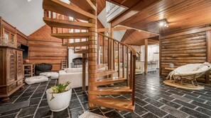 A log cabin interior with a spiral staircase, stone flooring, and rustic furnishings. - Crescent Lodge 307 Loftus Rd (CRESCENT HEAD)