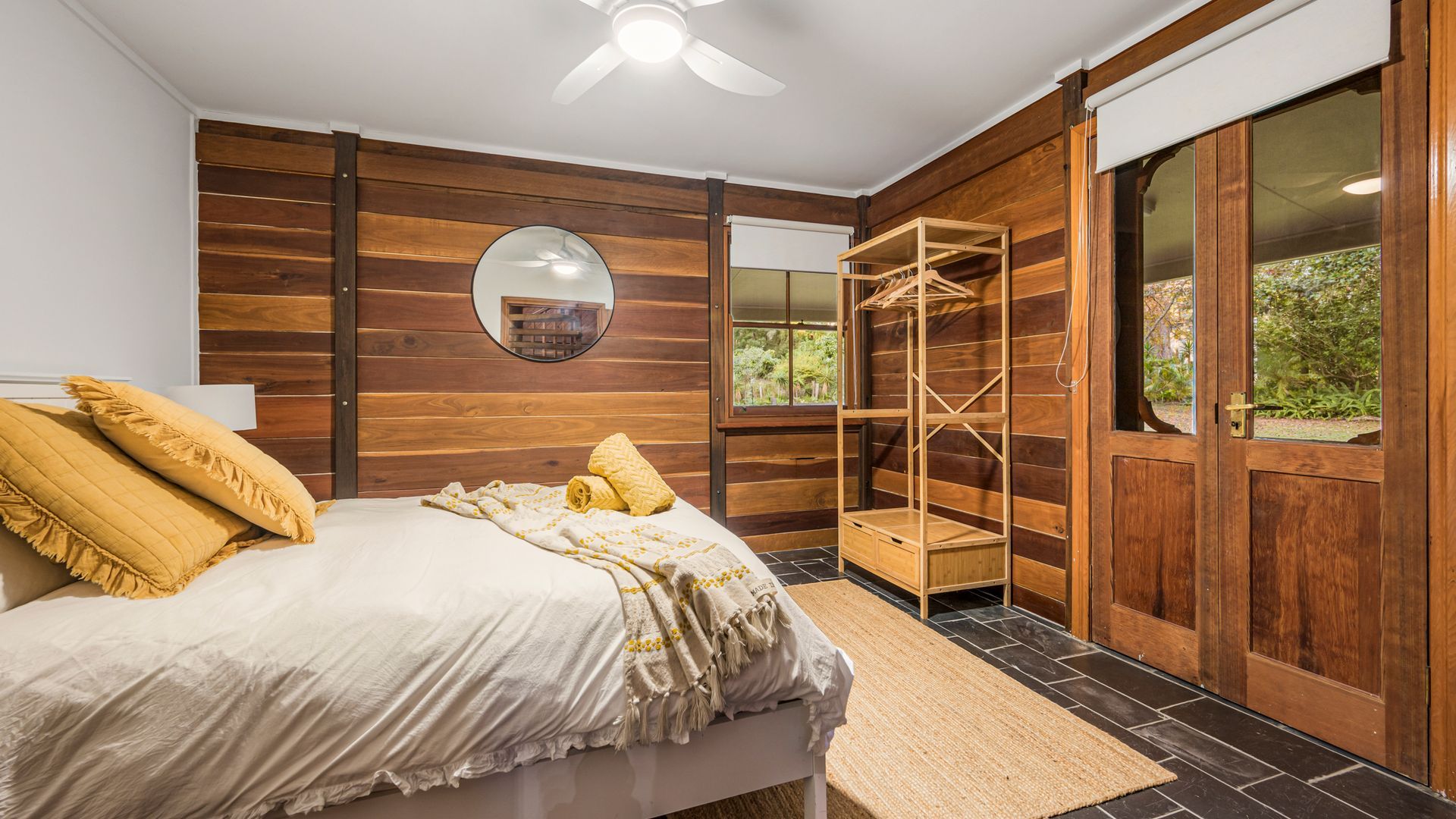 A bedroom with a bed, a wooden wardrobe, a mirror, and a window.
