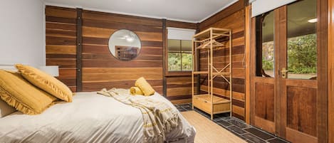 A bedroom with a bed, a wooden wardrobe, a mirror, and a window.