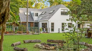 Una casa bianca con tetto spiovente, diverse finestre e un cortile recintato con tronchi e rocce.