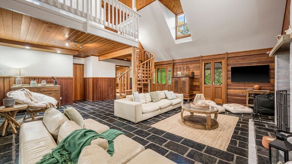 A spacious living area with a high ceiling, a built-in fireplace, and a large window providing natural light.
