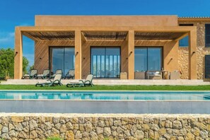 Ein modernes Haus mit Swimmingpool, Sitzgelegenheit im Freien und einer Steinmauer.