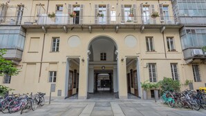 A building with a central archway, multiple balconies with potted plants, and bicycles parked outside. - Carlo Alberto House by Wonderful Italy (Torino)
