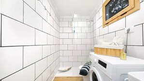 Ein kleiner Waschraum mit weiß gefliesten Wänden, einer Waschmaschine und einem Wäscheständer.