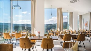 Un restaurant offrant une vue sur la montagne, doté d’un mobilier moderne et de grandes fenêtres.