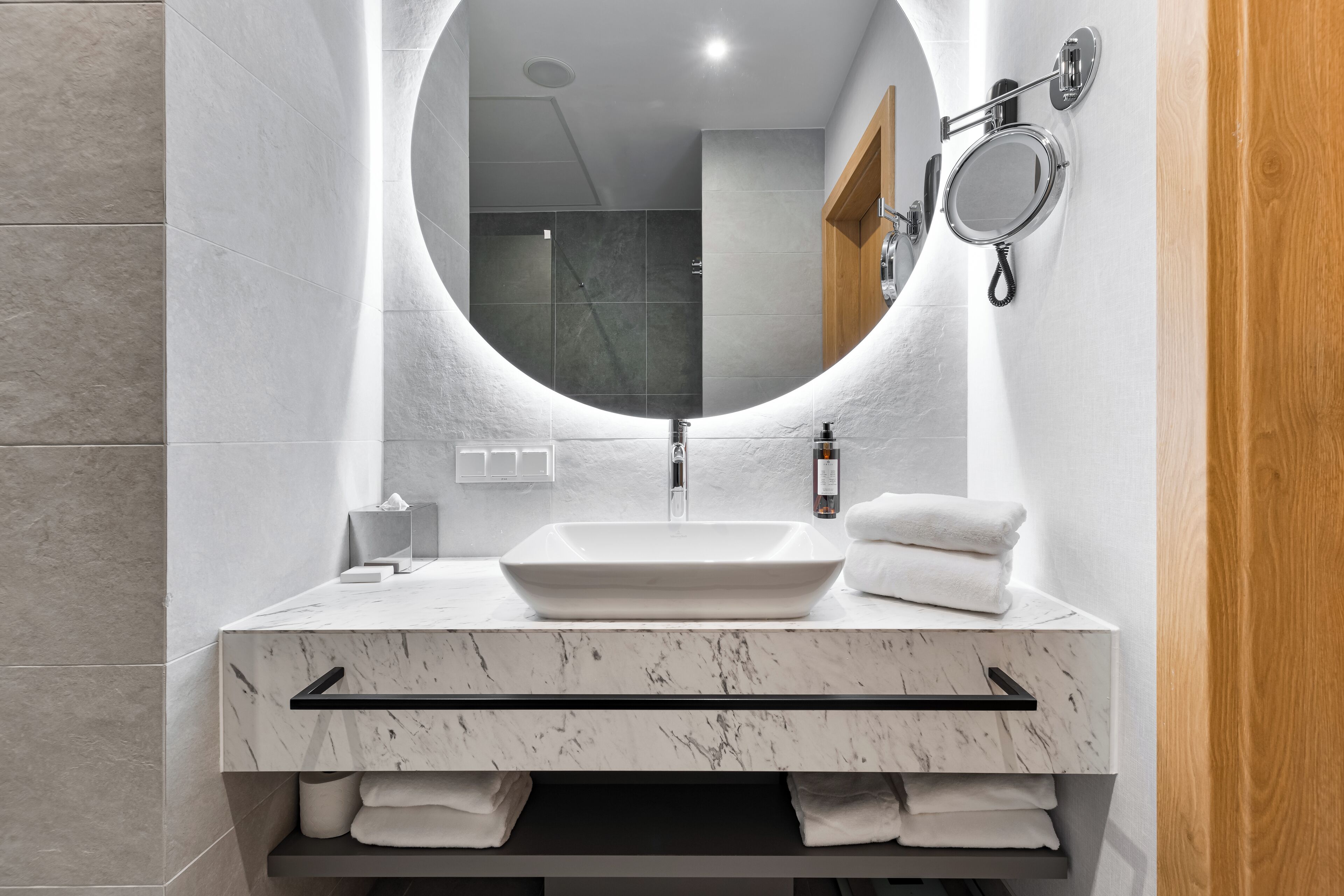 A modern bathroom with a large oval mirror, a rectangular sink, and a towel rack.