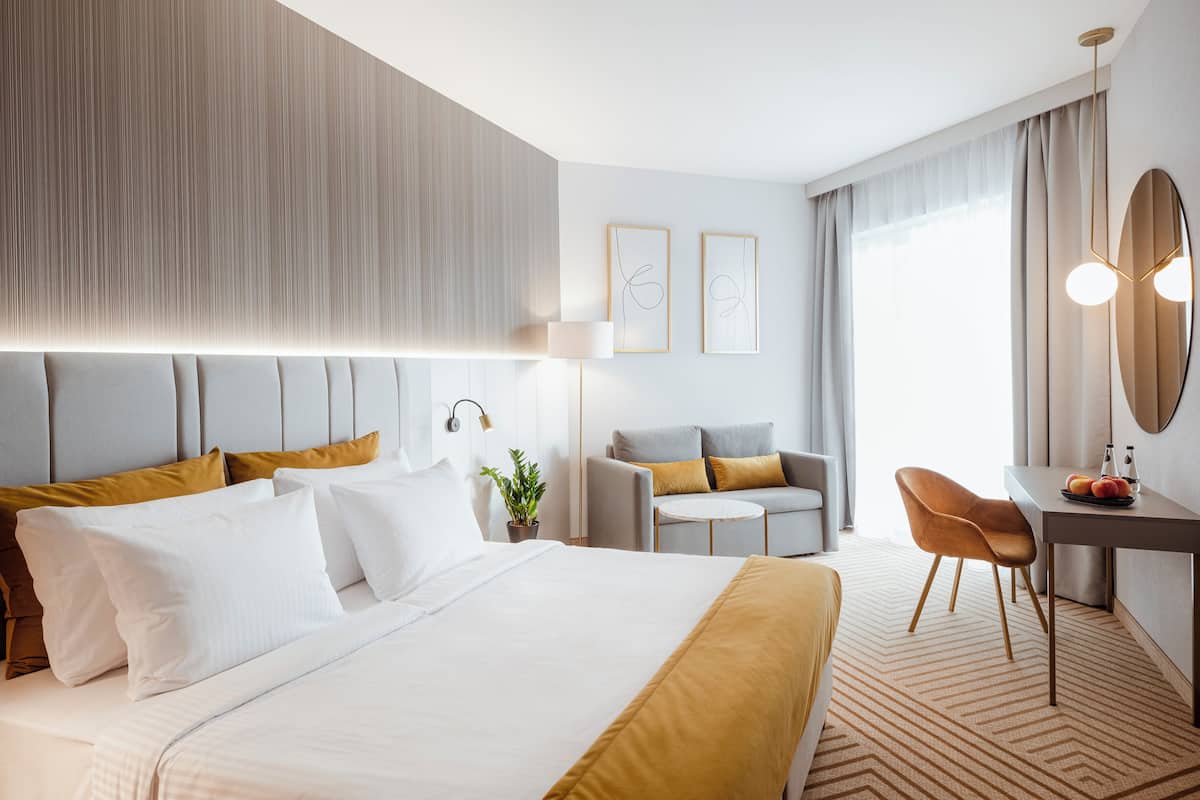 Una habitación de hotel moderna con una cama grande, un escritorio con una silla, una mesita y una planta en maceta.