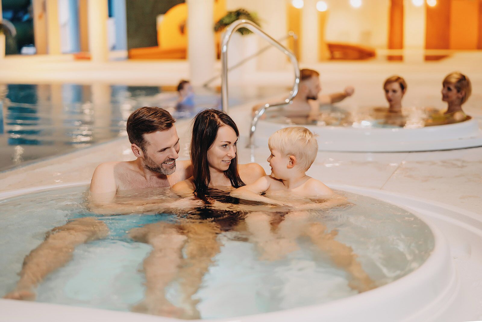 A family in a hot tub with a pool in the background.