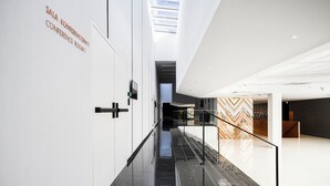 Un intérieur moderne avec une rambarde en verre, une signalétique pour la salle de conférence et un mur orné d’un motif.
