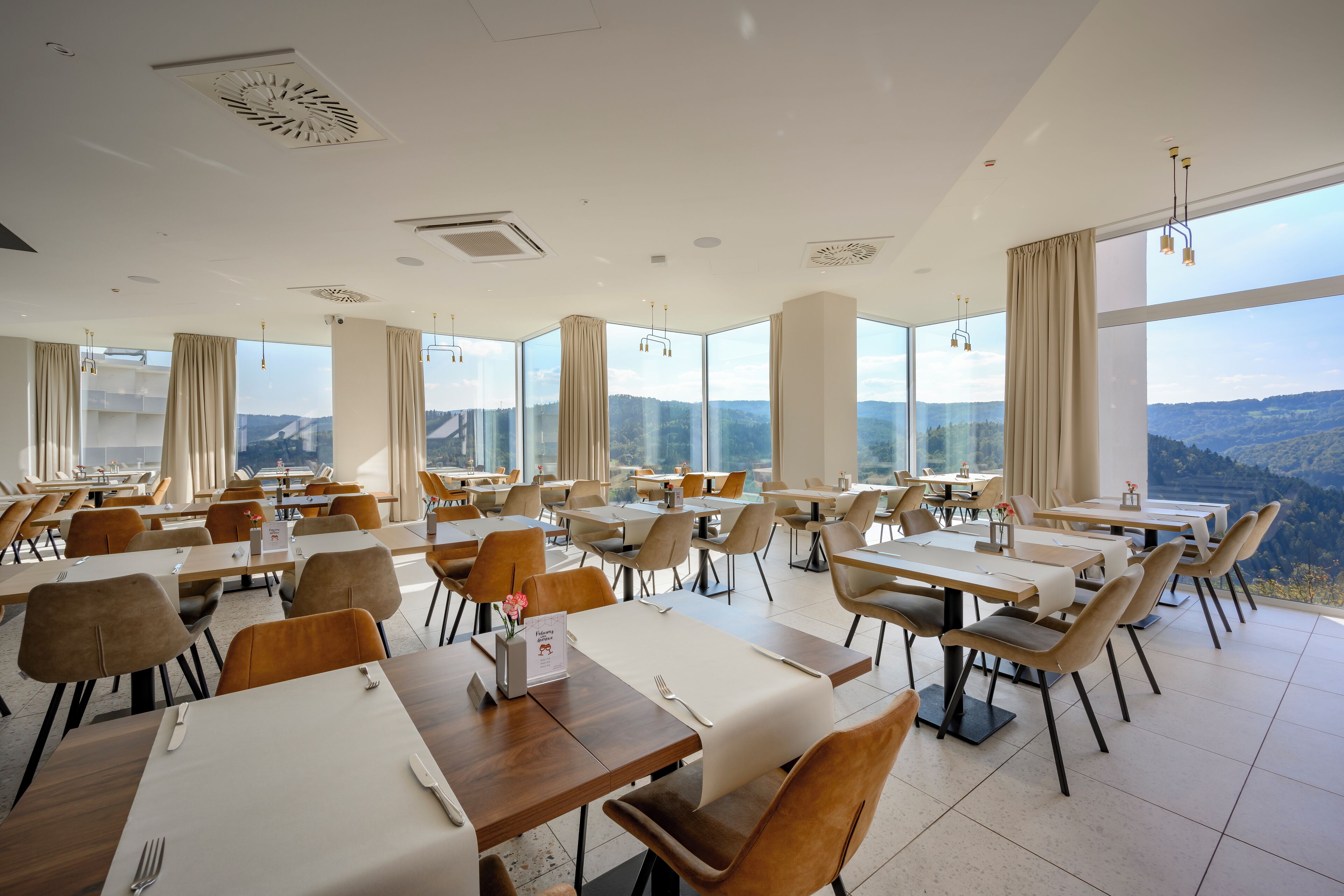 Un comedor amplio con varias mesas y sillas, y ventanas grandes que ofrecen vistas a las montañas.