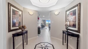 A hallway with framed artwork on the walls, a decorative floor pattern, and a view into a dining area.