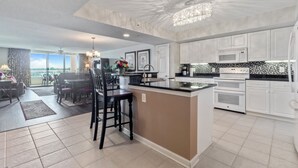 A modern kitchen with white cabinetry, a central island, and a dining area with a view.