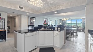 A modern kitchen with white cabinetry, a black countertop, and a large island. There is a dining area with a view of the outdoors.