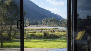 Vista de un paisaje natural con una montaña al fondo, una masa de agua y dos canguros en el césped.