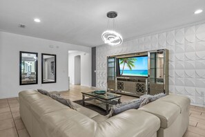 Un salon moderne avec un canapé en cuir, une table basse en verre et un téléviseur diffusant une scène de plage.