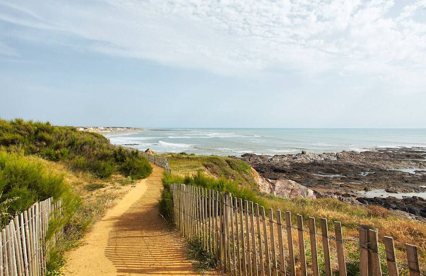 A coastal path leading to the beach with a wooden fence on one side and rocky terrain on the other.