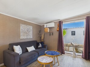 A modern living room with a grey sofa, two round tables, and a large window with curtains.