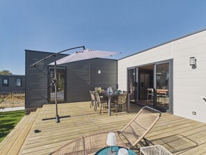 A modern outdoor deck with a dining table and chairs, a large umbrella, and a pool table.