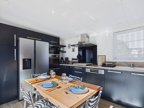 A modern kitchen with a dining area, featuring a refrigerator, oven, and coffee maker.