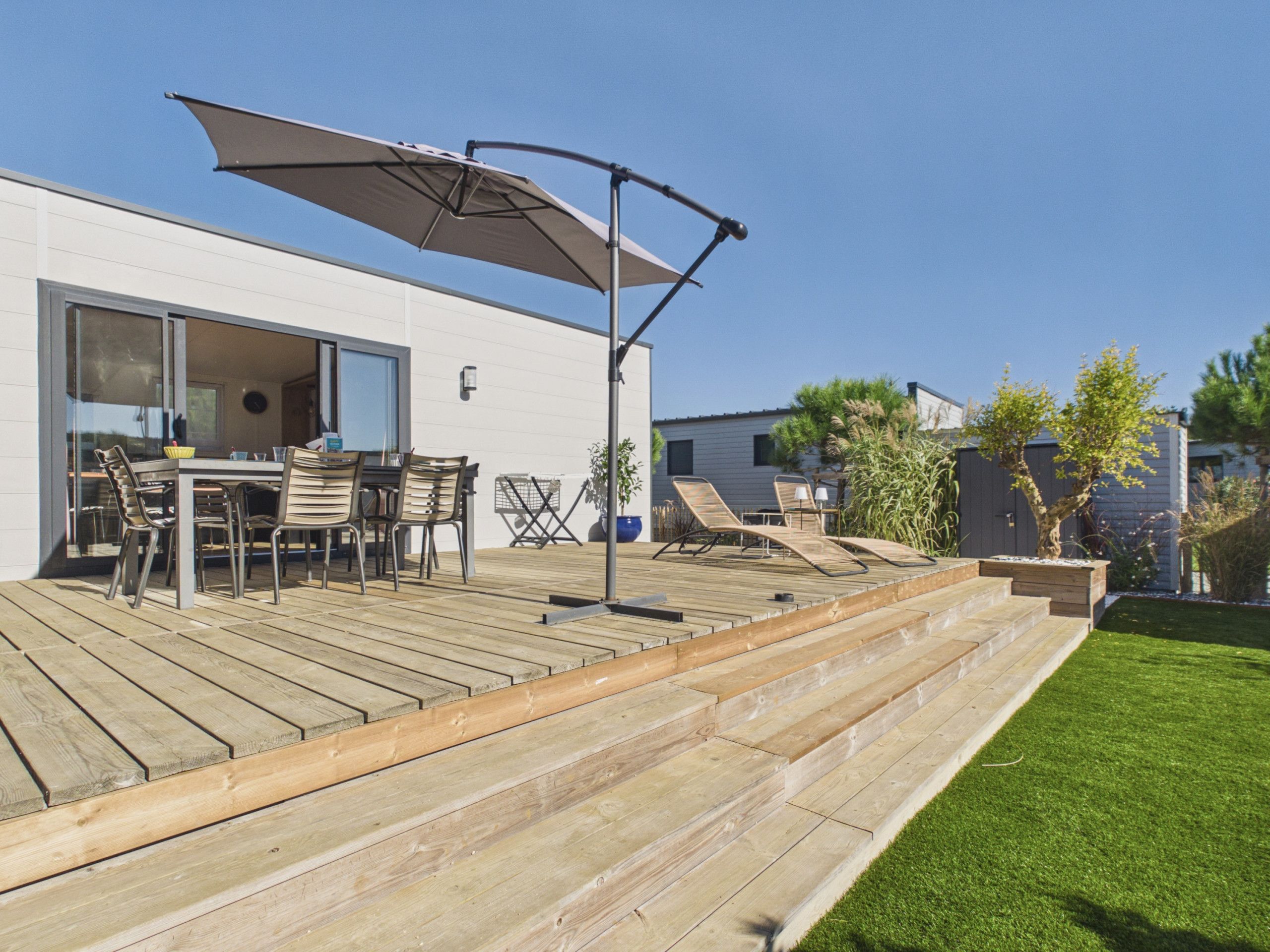 Una terraza de madera con mobiliario exterior, una mesa y una sombrilla grande.