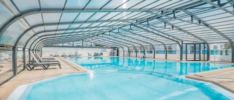 An indoor swimming pool with a glass ceiling, lounge chairs, and a lifeguard stand.