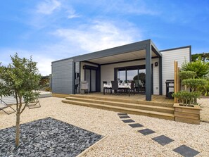 Une maison moderne dotée d’un patio couvert, d’une allée en gravier et d’un petit jardin.