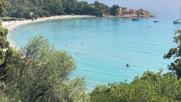 Una playa costera con aguas turquesas cristalinas, embarcaciones y un acantilado rocoso.