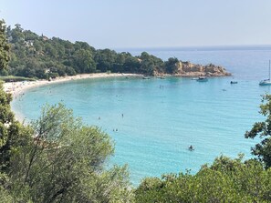 A coastal beach with clear turquoise waters, boats, and a rocky cliff. - Maison Individuelle Dans Résidence Familiale à 700m à Pied de la mer (Ghisonaccia)