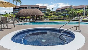 A swimming pool area with lounge chairs and a hot tub, surrounded by a building with a tiled roof and palm trees. - Keauhou Punahele A103 | Ground Floor Condo with Split AC and Oceanviews (Kailua-Kona)