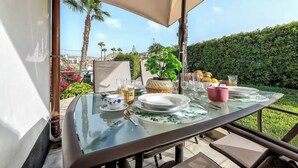 An outdoor dining table with a glass top, surrounded by chairs and a large umbrella.