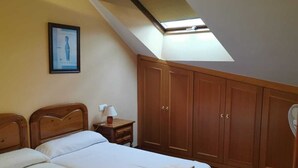 A bedroom with two beds, wooden wardrobe, a bedside table with a lamp, and a skylight. - Apartamento Cinema (Cangas de Onís)