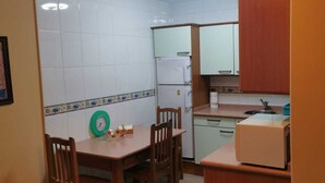 A compact kitchen with white tiled walls, a wooden dining table with four chairs, a refrigerator, a sink, and wooden cabinets. - Apartamento Cinema (Cangas de Onís)
