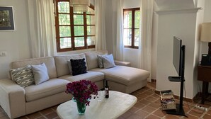 A living room with a sofa, a coffee table with a vase, a TV, and a window with curtains.