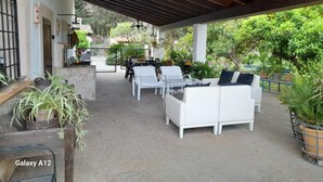 An outdoor patio area with white furniture, including sofas and chairs, under a wooden pergola.