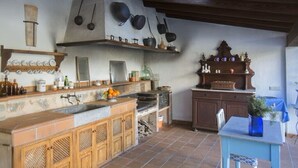A rustic kitchen with wooden cabinets, a stone countertop, and hanging pots.