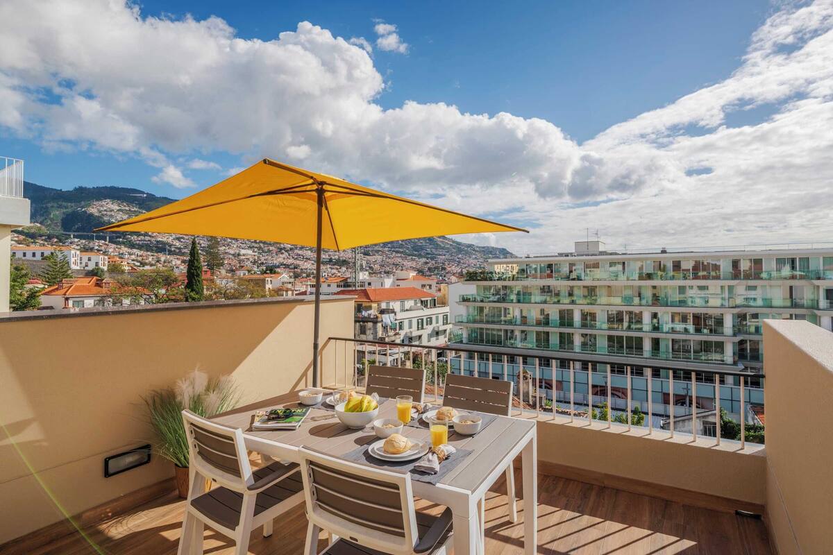 A balcony with a table set for breakfast, overlooking a cityscape and mountains.