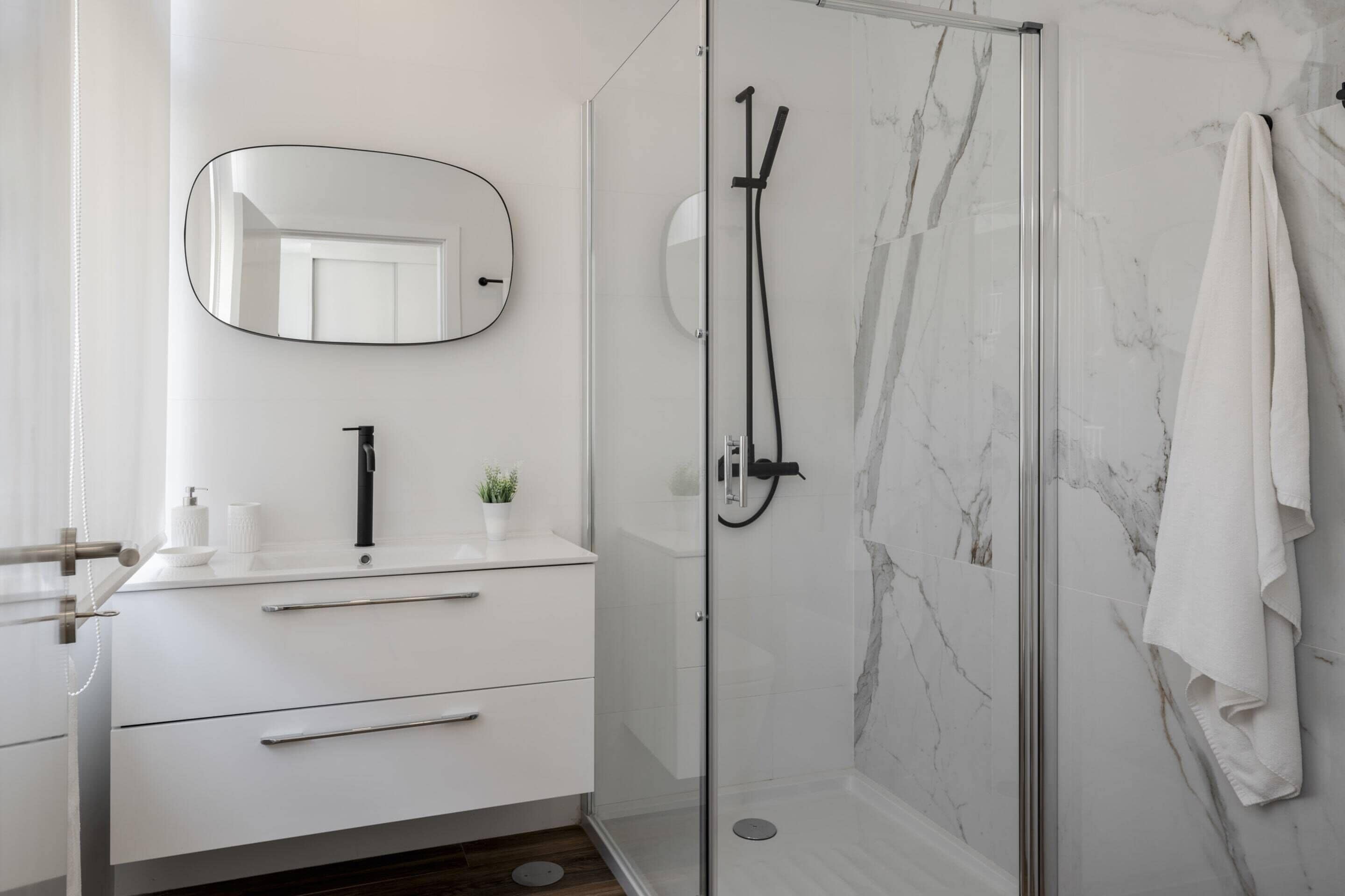A modern bathroom with a glass-enclosed shower, a white vanity with a mirror, and a marble wall.