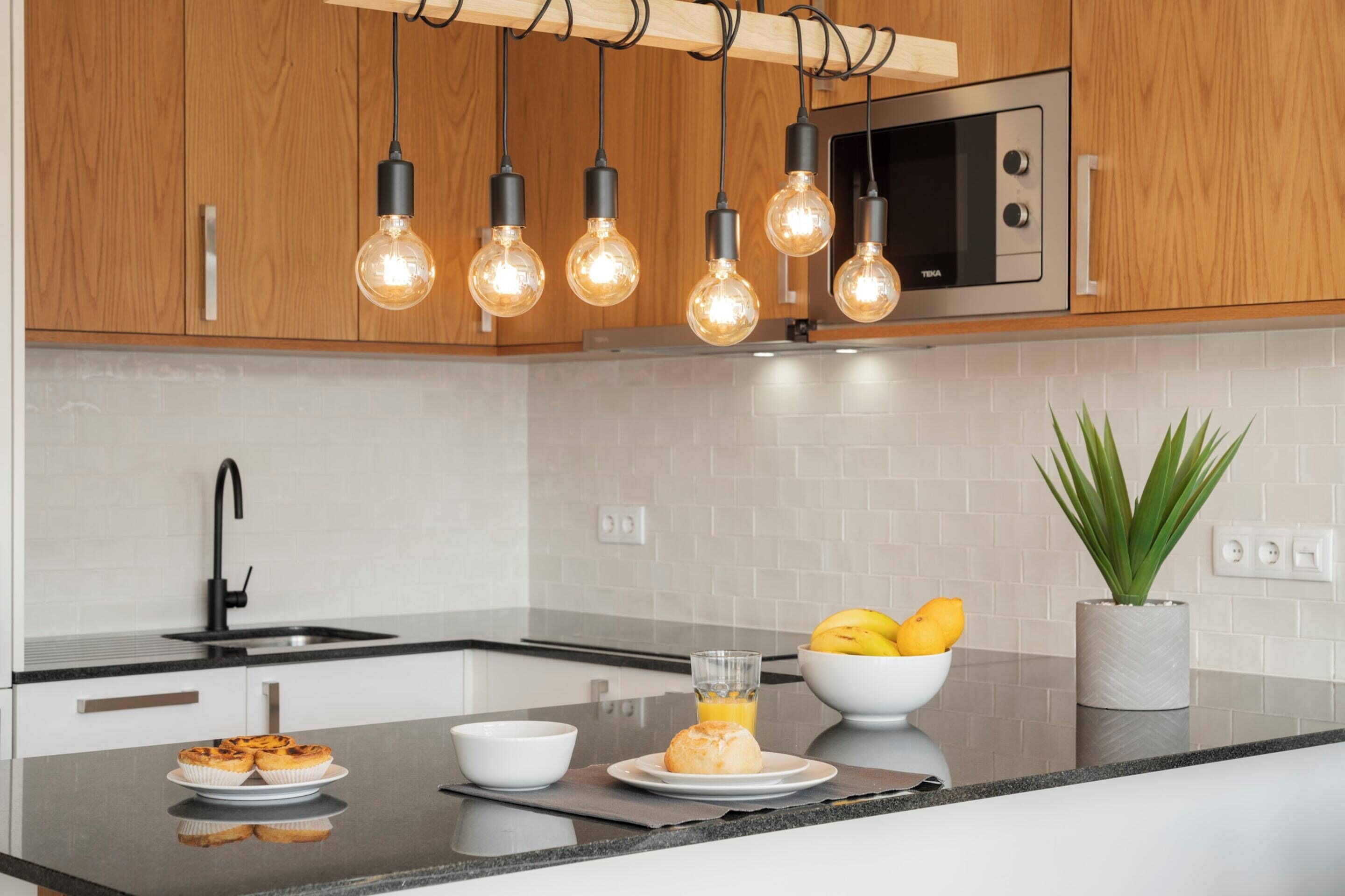 A modern kitchen with wooden cabinets, a stainless steel microwave, and a black faucet.