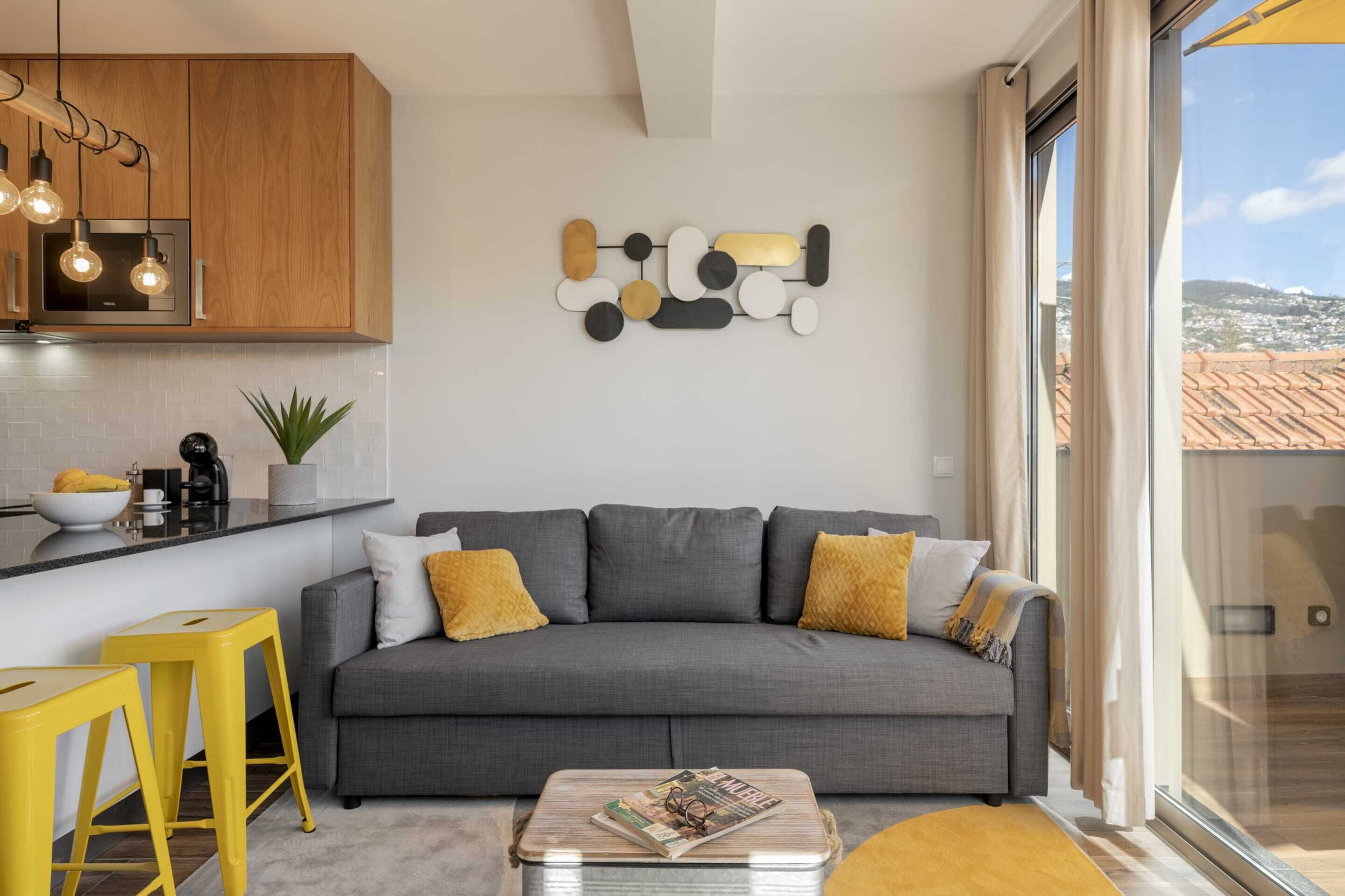 Un salon moderne avec un canapé gris, des tabourets jaunes et un magazine posé sur une table basse.
