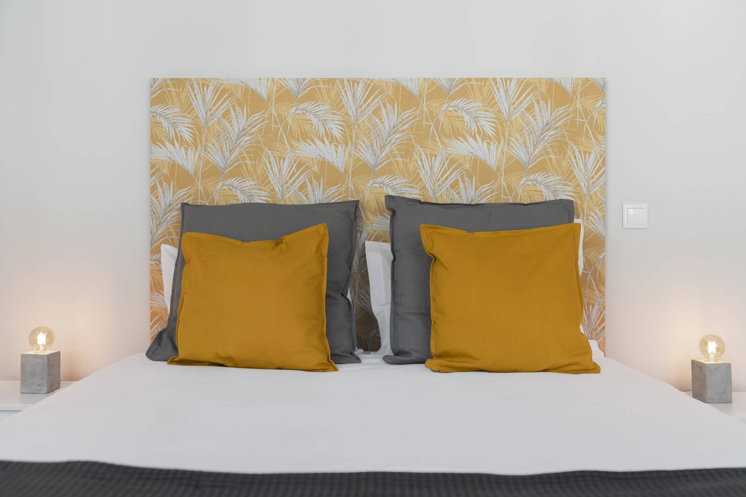 A neatly made bed with two pillows, a headboard with a leaf pattern, and bedside lamps.
