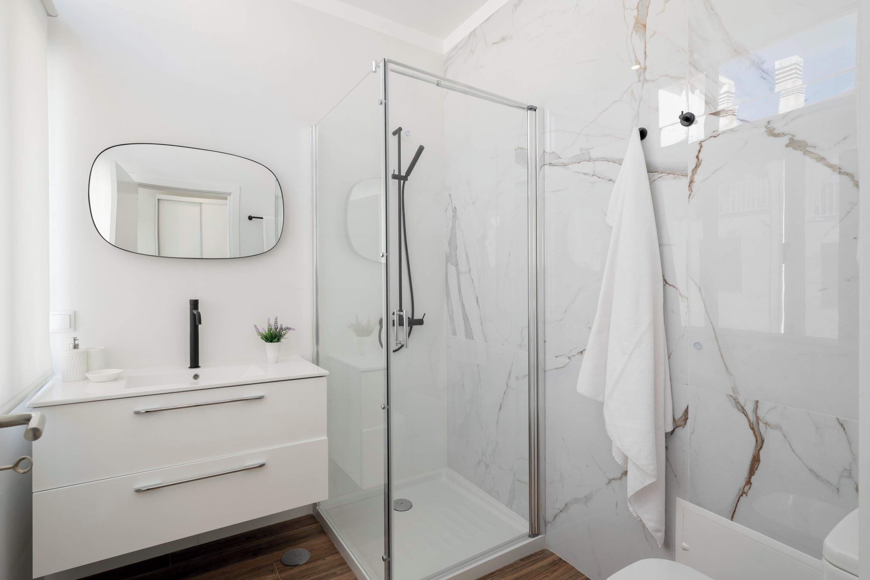 A modern bathroom with a glass-enclosed shower, a white vanity with a mirror, and marble walls.